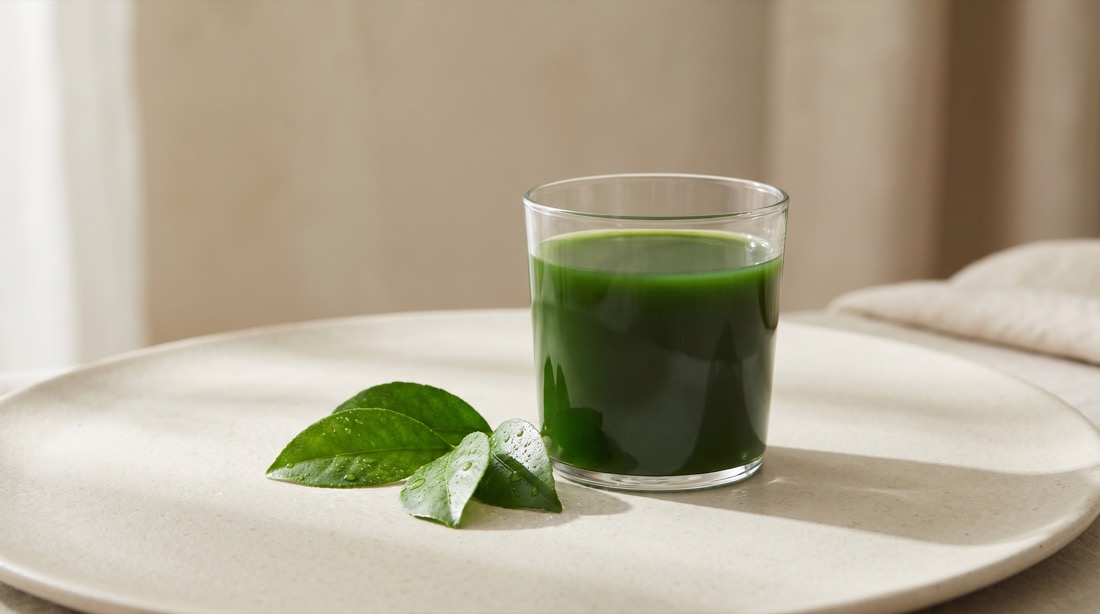 A glass of deep-green chlorophyll liquid beside fresh green leaves
